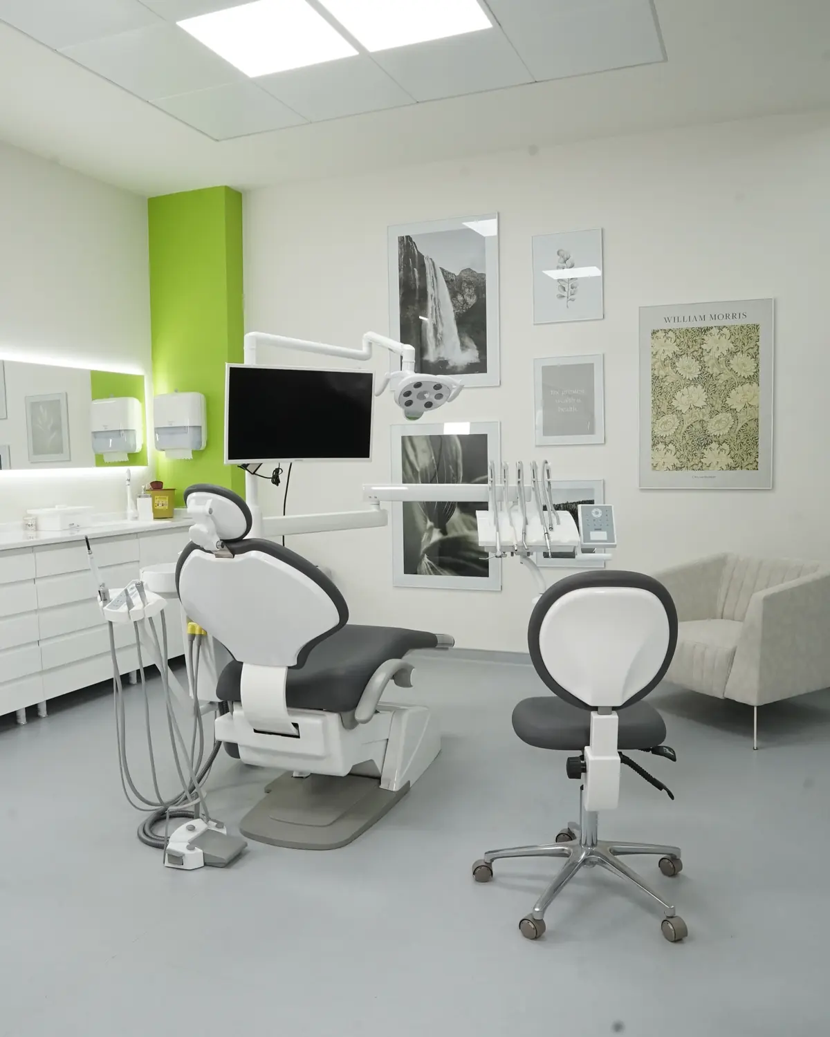 Behandlungszimmer mit Behandlungsstuhl, Bildschirm am Stuhl und Arzthocker